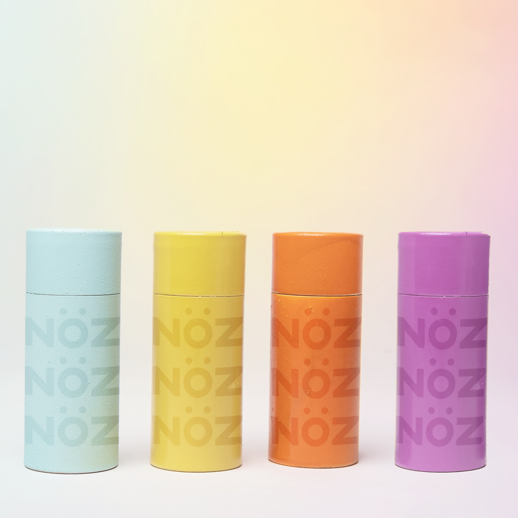 Four colorful Nöz Sunscreen sticks side-by-side in shades Teal Yellow Orange and Purple